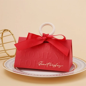 Detail of red triangular wedding favor box with a wooden ring handle and happy moment text