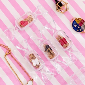 Cute candy-shaped transparent storage boxes with golden jewelry on pink striped background