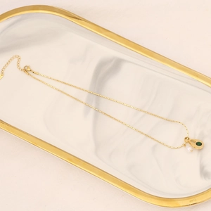 Golden butterfly necklace with emerald heart and white pearl pendant on marble tray