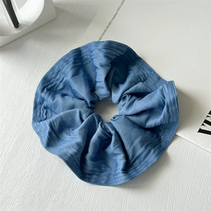 Detailed view of blue denim fabric scrunchie with soft ruffled texture on wooden background