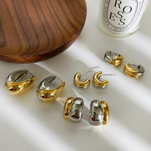 Modern two-tone gold and silver drop and C-shaped earrings set on minimalist background