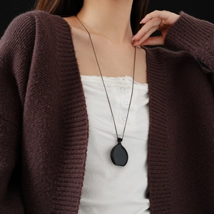 Detail of tear-drop faux wood pendant necklace worn with a brown knit cardigan