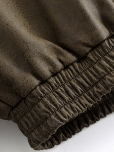Close-up of brown faux leather jacket sleeve showing vintage texture and elastic cuffs