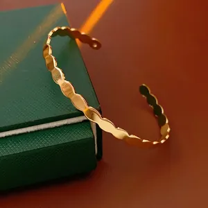 Minimalist gold wavy open bangle with polished geometric design on a green jewelry box
