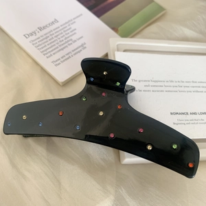 Elegante pinza per capelli in acetato nero con strass colorati su sfondo beige