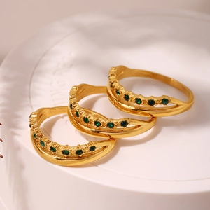 Set aus drei geschichteten goldenen Edelstahlringen mit grünen Zirkonia auf weißem Sockel