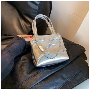 Detail view of silver metallic handbag with decorative bows and elegant pearl chain