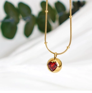 Détail de la chaîne serpent dorée avec rubis en cœur sur un pendentif sphérique