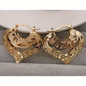 Macro shot of gold heart hoop earrings with intricate hollow-out patterns on velvet