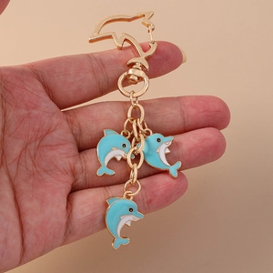Golden dolphin keychain with three blue enamel pendants shown in hand for size