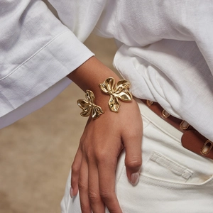 Gold open bangle with layered floral butterfly design worn on wrist over linen outfit