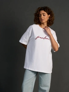 Λεπτομέρεια από λευκό βαμβακερό oversized μπλουζάκι με κόκκινη στάμπα freedom και υφή