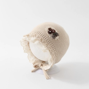 Detail view of beige baby knit hat with lace trim and decorative plaid flower bow