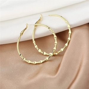 Detailed close-up of gold textured hoop earrings with a wavy metallic surface design