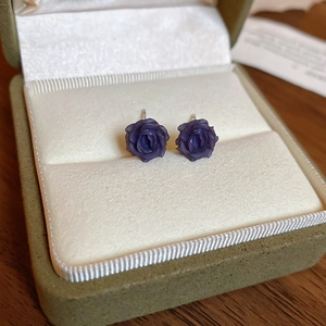Vue macro de boucles d'oreilles roses mauves en résine sur satin blanc en boîte à bijoux
