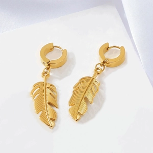 Macro detail of golden feather pendant earrings on white stone and silk background