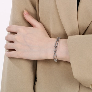 Silver paperclip and twist link chain bracelet worn on wrist over a beige blazer