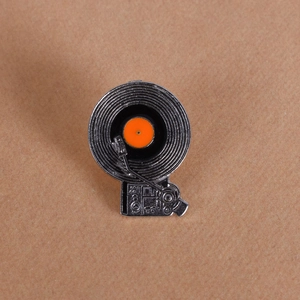 Detail of vintage vinyl record player enamel pin with orange center on textured paper