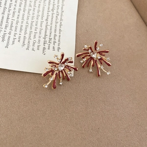 Detail of red and gold firework earrings with zircon inlay on a warm textured background