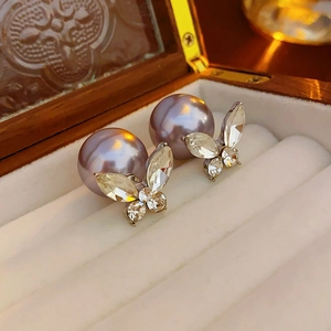 Gros plan d'une boucle d'oreille papillon avec perle violette dans un coffret à bijoux