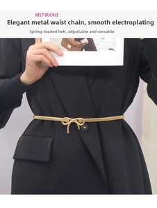 Detail view of a gold metal elastic waist chain with a delicate bow buckle on a black suit