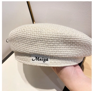 Close-up of cream white tweed beret featuring detailed woven texture and leather logo patch