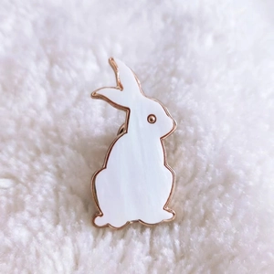 Detailed close-up of a white enamel rabbit brooch with a gold-tone metallic frame