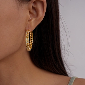 Detail view of gold Cuban link hoop earring with white zircon inlay on model ear