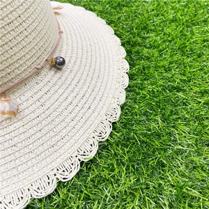 Détail d'un chapeau de paille avec bord ondulé, cordon rose, perles grises et coquillage