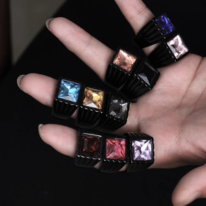 Macro shot of colorful square gemstones set in black stainless steel rings on a hand