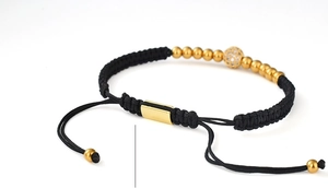Macro shot of 5mm gold beads and zircon-encrusted ball on a black braided bracelet