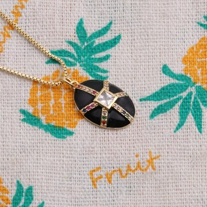Détail d'un collier plaqué or avec un pendentif ovale noir et une croix en gemmes colorées