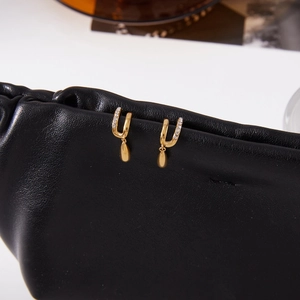 Gros plan de boucles d'oreilles double C dorées avec gouttes de zircon sur cuir