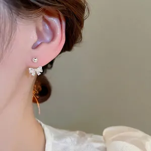 Sparkling zircon bow earrings with silver needles worn on ear, elegant jewelry style