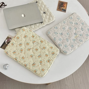 Detailed view of quilted laptop sleeves with floral patterns and bow on a white table