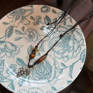 Detail of bohemian wooden bead necklace with silver grape pendant on floral ceramic plate