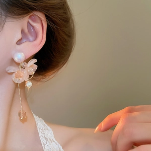 Dettaglio macro di orecchini a fiore rosa con lunghe nappe e perle indossati da modella
