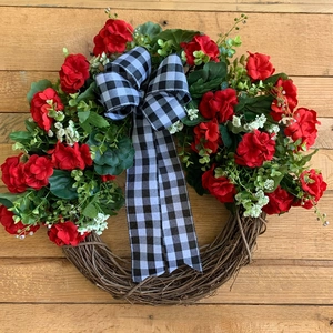 Detail of rustic Christmas wreath with red geraniums and black plaid bow on wood