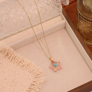 Detailed shot of star pendant necklace with pink stone and blue bead on a wooden tray