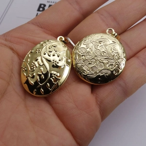 Hand holding floral engraved gold locket pendants in oval and round shapes