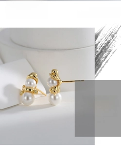 Macro detail of gold-plated snowman stud earrings with elegant white pearls on white stone