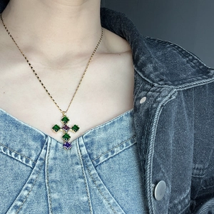 Detail of cross necklace with green and purple stones on gold chain worn by model