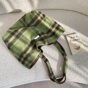 Detail of green plaid tote bag showing thick textured fabric on a white fleece sofa