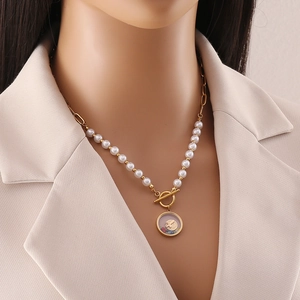 Gold pearl necklace with round cross pendant and colorful stones worn by a model