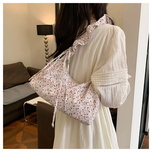 Detailed side view of floral canvas shoulder bag featuring ruffled straps and tassel drawstrings