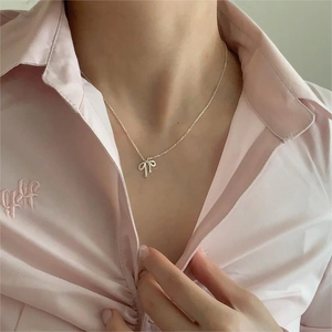 Detail of a minimalist 925 sterling silver bow pendant necklace worn on a model