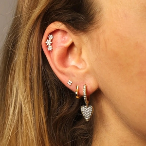 Detailed close-up of gold clover earrings and heart pendant set with sparkling zircons