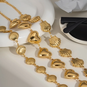 Detail of gold layered chain featuring heart and seashell charms on white porcelain