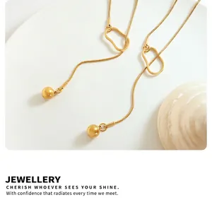 Macro detail of 18k gold plated snake chain with geometric ball pendant on a white surface