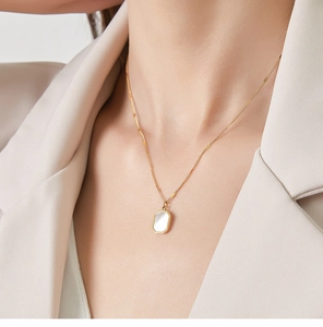 Detail of 18K gold titanium steel necklace featuring a rectangular white shell pendant on a model